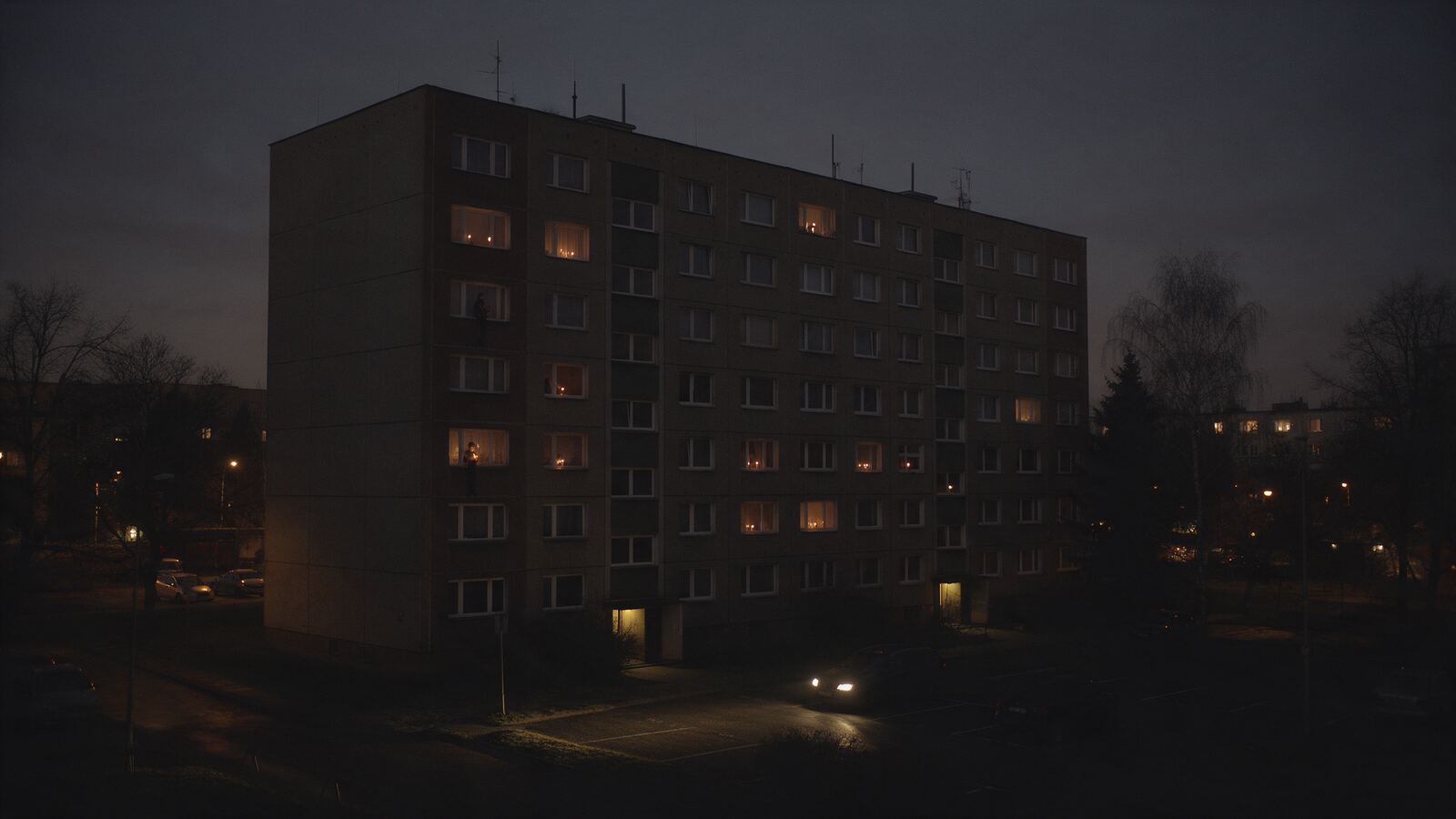 Panelák večer při výpadku proudu, jen pár oken svítí svíčkami
