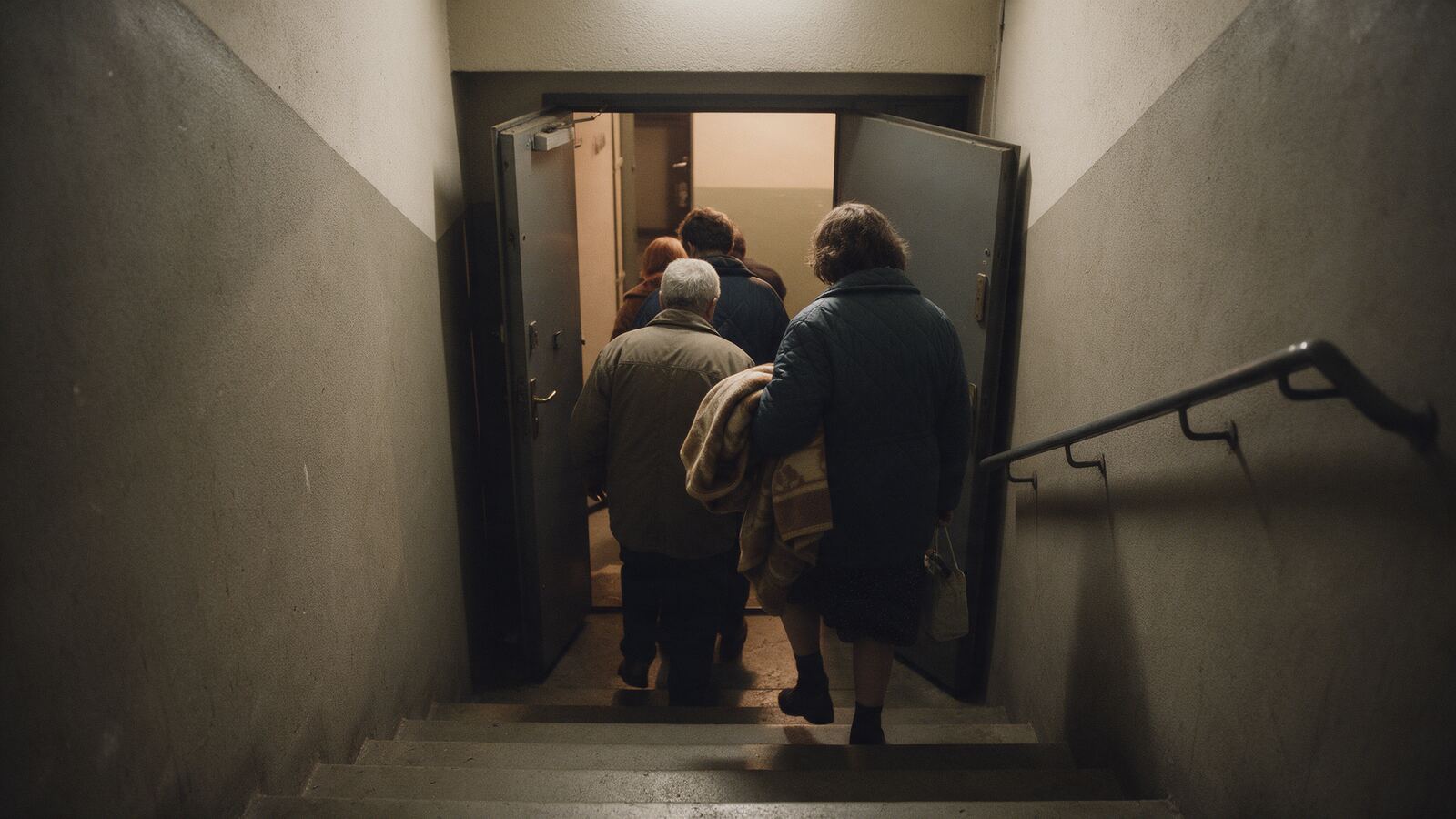 Lidé zezadu klidně scházejí po schodech do sklepa paneláku